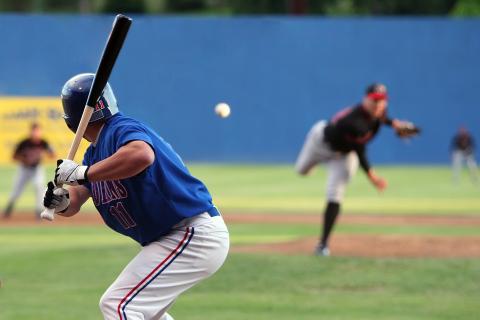 In a view from behind home plate, you see a pitcher releasing a baseball toward the waiting batter.